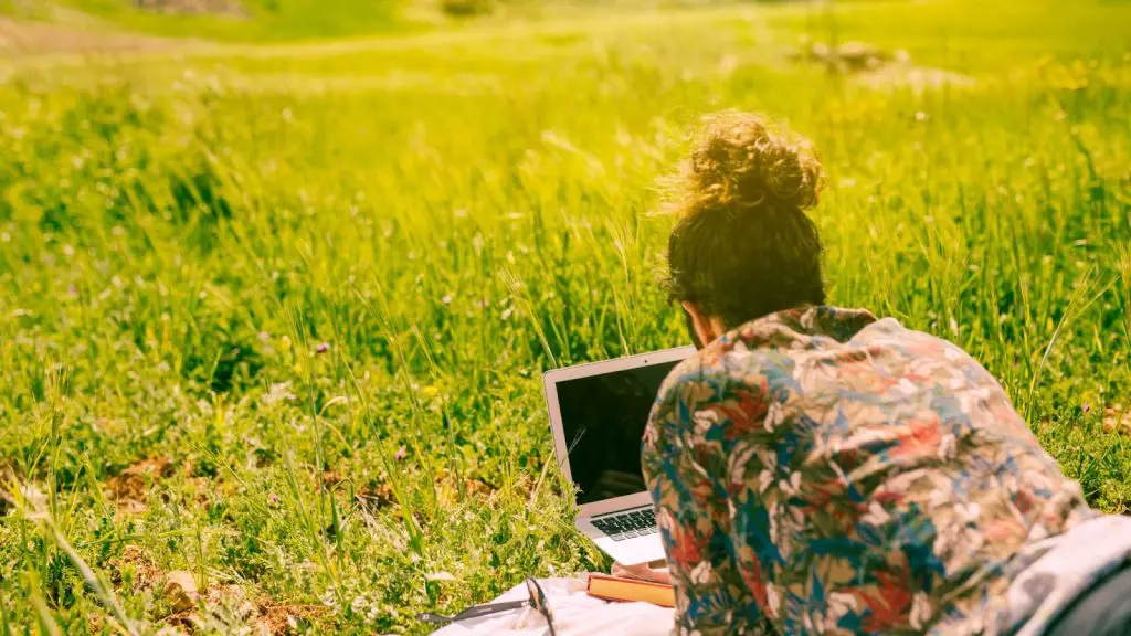 мъж работи на лаптоп легнал на зелена поляна