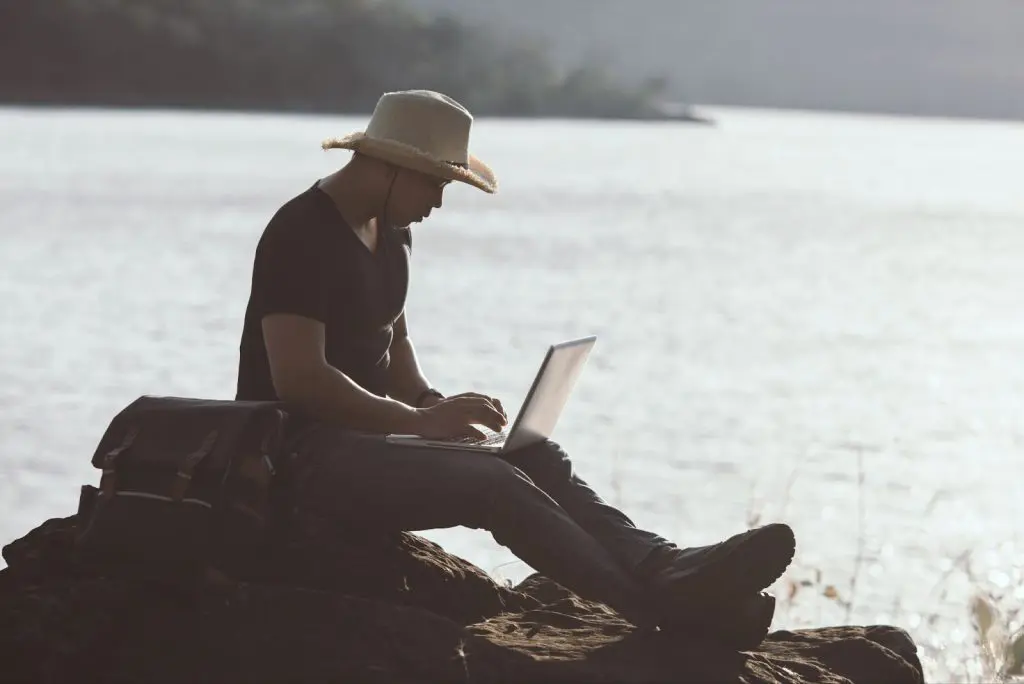 мъж със сламена шапка работина сред природата на лаптоп