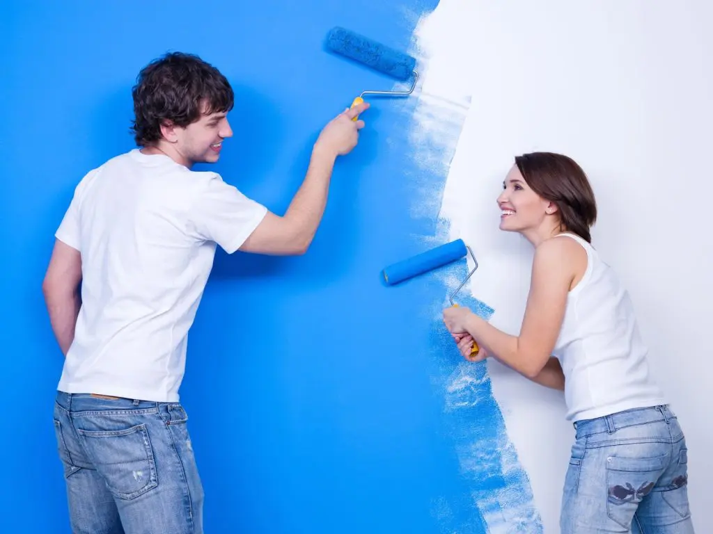 мъж и жена боядисват стена в син цвят